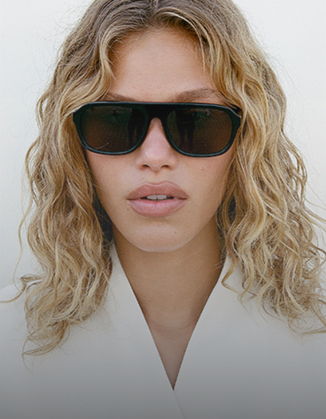 Woman wearing aviator style sunglasses with a neutral background