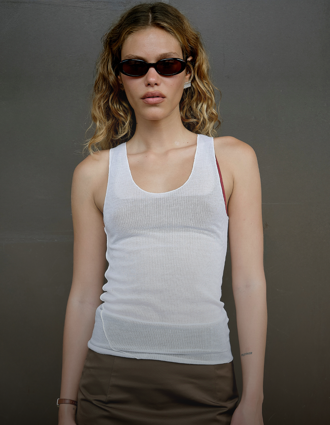 Woman wearing a white tank top and sunglasses against a plain background